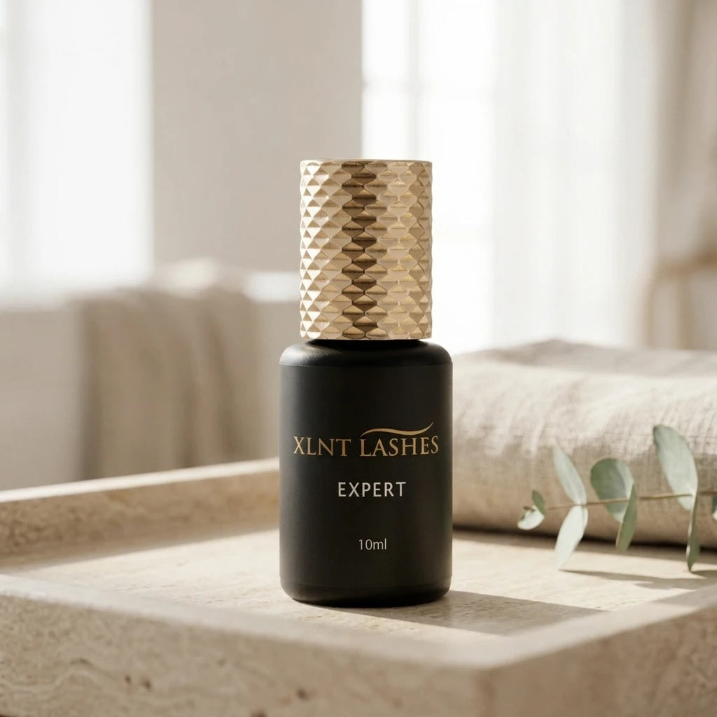 Expert Glue 10ml 1 Sek i matt svart flaska med mönstrad guldkork på en beige stenbricka med eukalyptusblad.