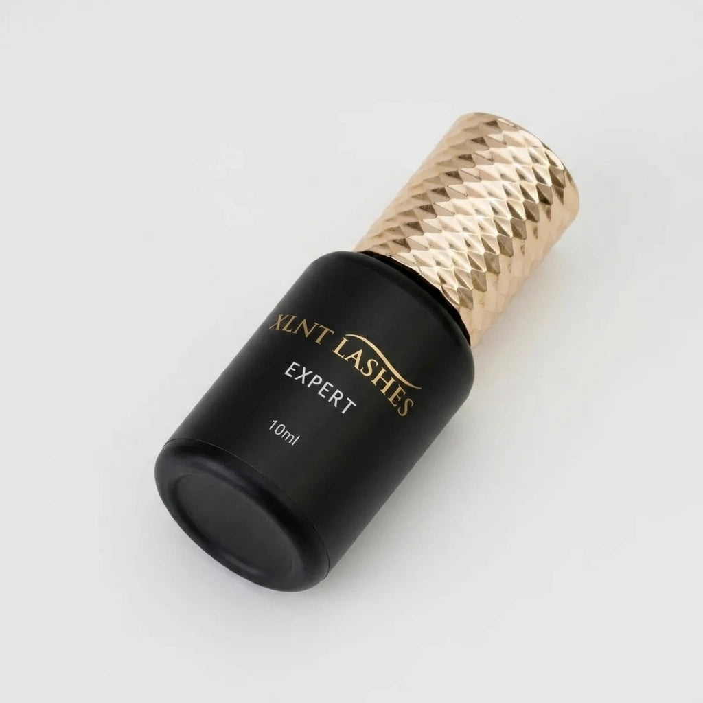 Svart flaska med mönstrat guldlock för franslimmet Expert Glue 10ml 1 Sek från XLNT Lashes på ljus bakgrund.