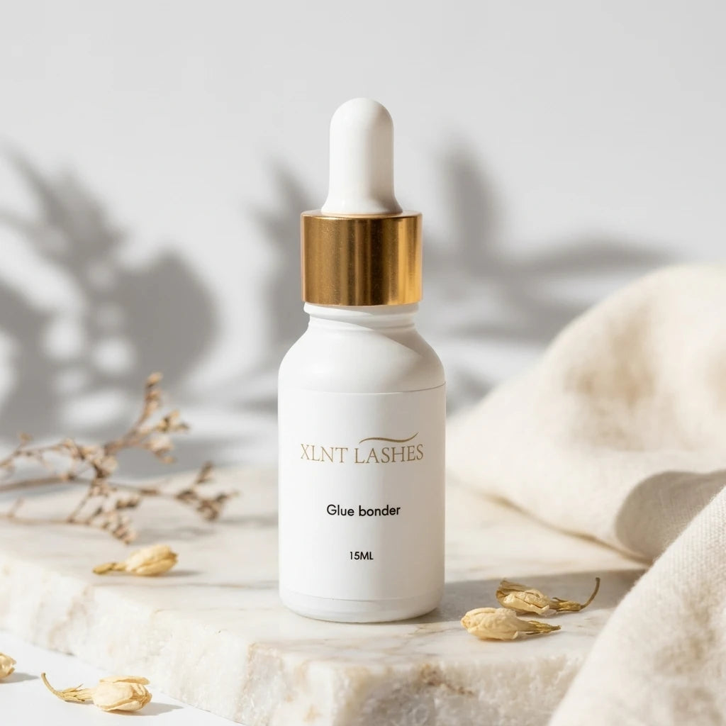 XLNT LASHES Eyelash Extension Glue Bonder 15ml white dropper bottle with gold cap on marble.
