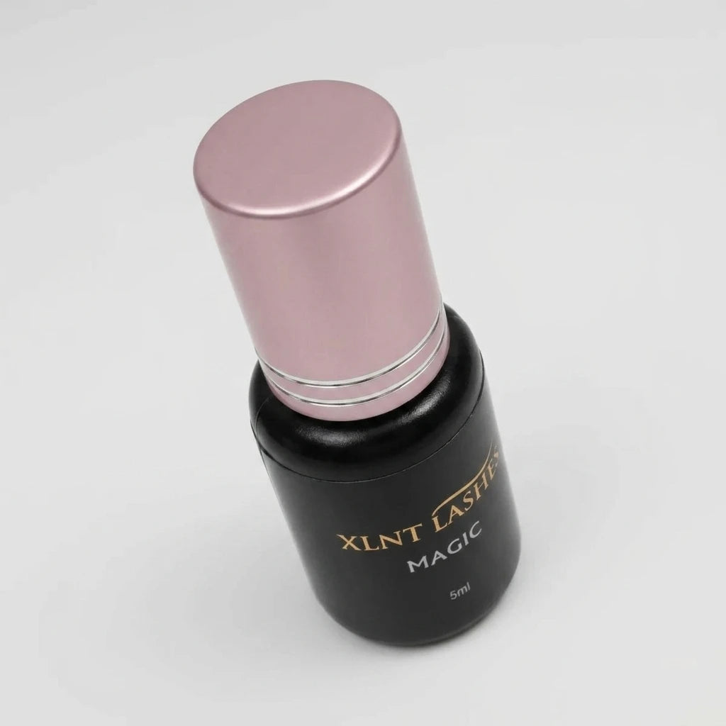Magic Glue 5ml - 02-1 Sek i svart flaska med guldskrift och metalliskt rosa kork mot en ljusgrå bakgrund.