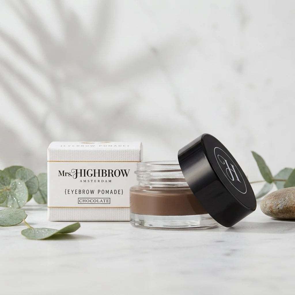 Öppen glasburk med Mrs. Highbrow Eyebrow Pomade i brun ton och vit ytterförpackning på ljus marmoryta.