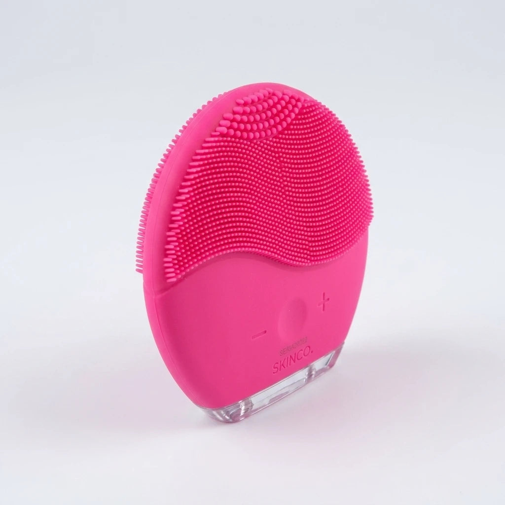 Oval rosa facial cleanser brush med mjuka borststift och reglerknappar, vänster vinkel mot vit bakgrund.