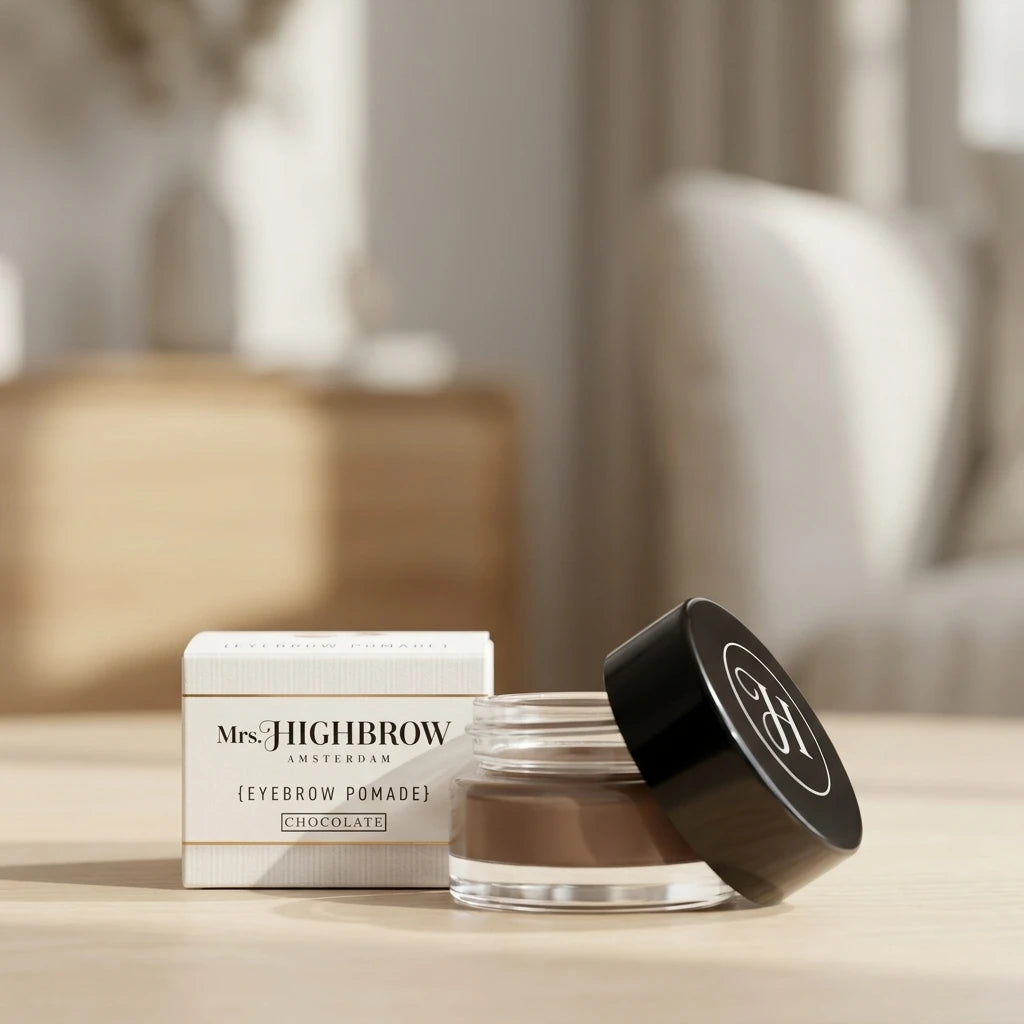 Mrs. Highbrow Eyebrow Pomade Chocolate i glasburk bredvid vit kartong, fotograferad på ett träbord.