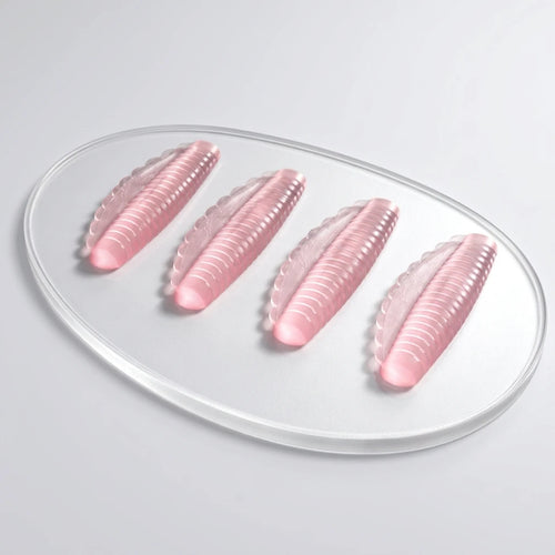 Fyra rosa, räfflade Korean Lash lift spole Pinky i silikon på en transparent oval platta mot en ljus bakgrund.