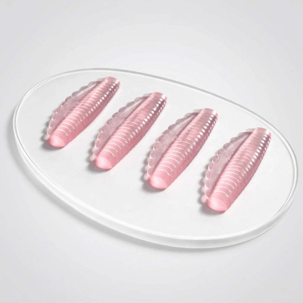 Fyra rosa, räfflade silikonspolar av modellen Korean Lash lift spole Pinky på en transparent oval platta.