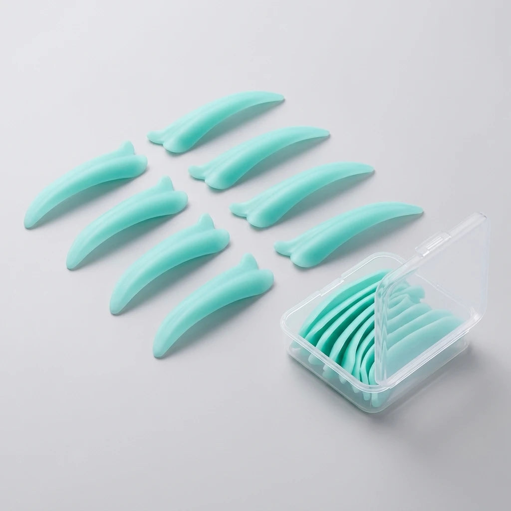 Mintgröna silikonformar av Korean Lash lift spole Dolphin placerade bredvid en transparent plastbox på grå bakgrund.