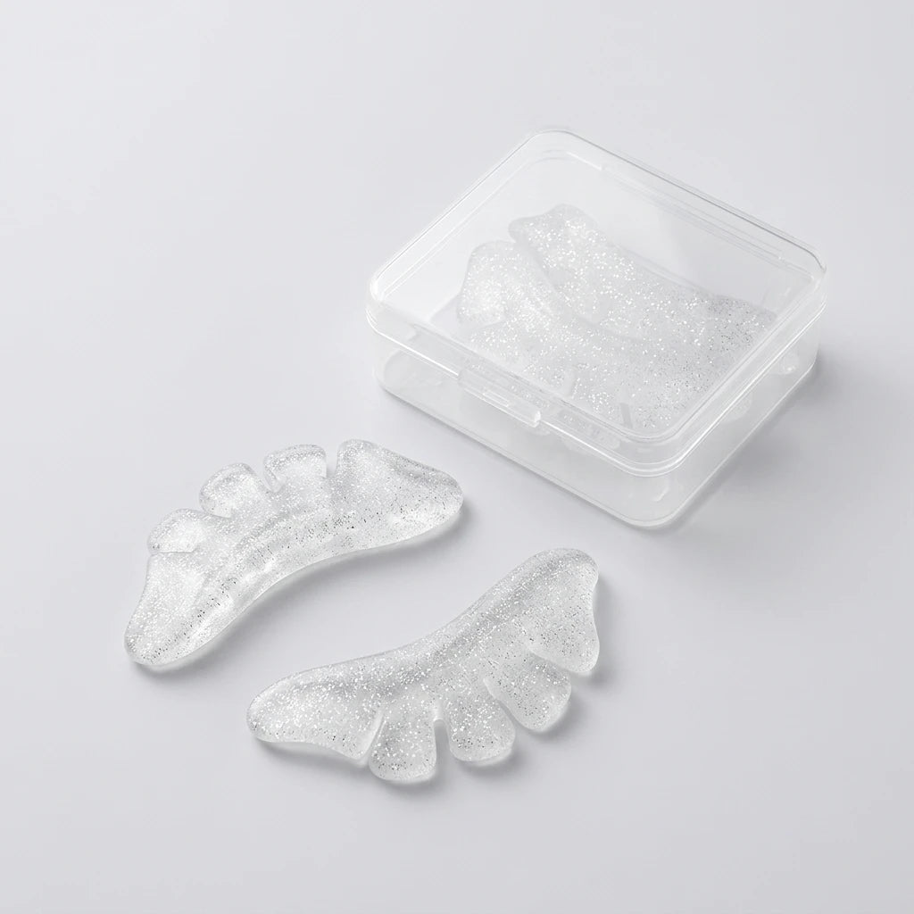 Glittrig Korean Lash Lift Spole Underfransar Butterfly i transparent silikon bredvid en plastask på ljusgrå yta.