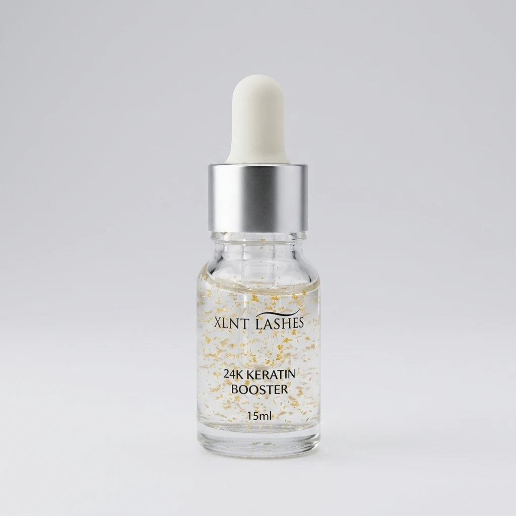 XLNT LASHES 24k Essence 15ml i klar glasflaska med guldflagor, pipett och silverlock mot ljus bakgrund.