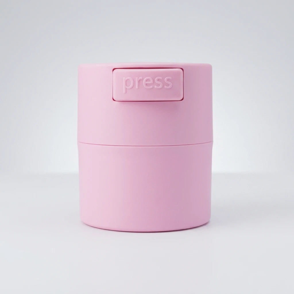 Rosa cylinderformad Glue Box i matt plast med pressknapp på locket, mot ljus neutral bakgrund.