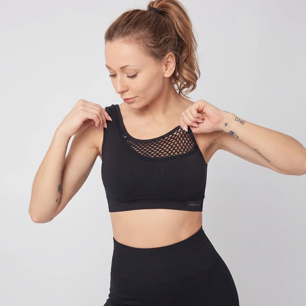 Kvinna bär svart Contour Mesh Sport-BH med nätmönstrad detalj vid ringningen, ljusgrå bakgrund.