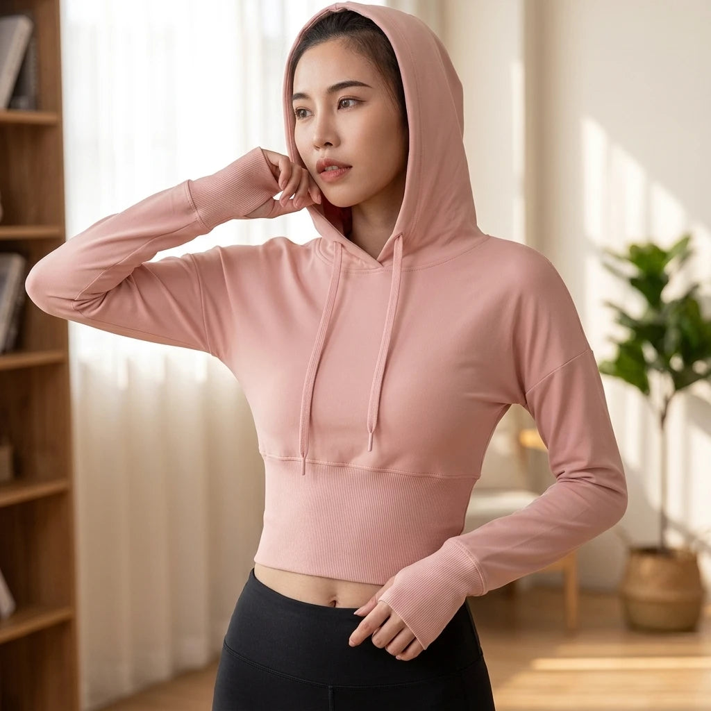 Kvinna i puderrosa croppad hoodie med ribbad midja och svarta tights i ljus hemmiljö, sedd framifrån.