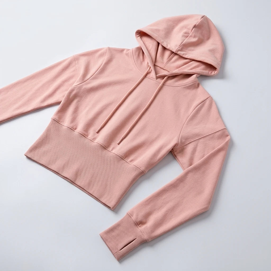 Croppad hoodie puderrosa i närbild med dragsko, bred ribbad mudd och mjukt stretch-material