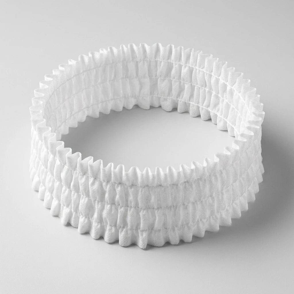 Rynkat vitt engångshårband i mjukt nonwoven-material mot ljusgrå bakgrund, sett från vänster