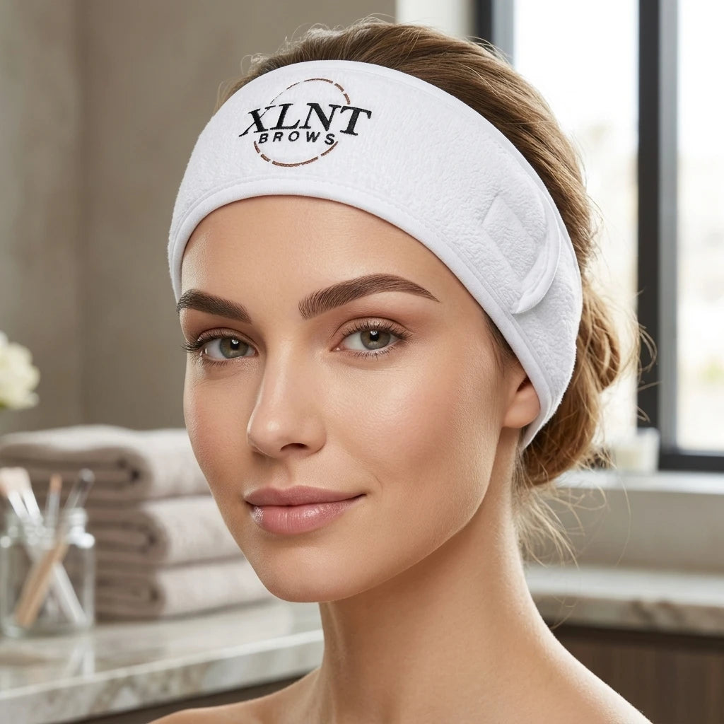 Kvinna bär vitt XLNT Brows frottéhårband under behandling i ljus salongsmiljö.