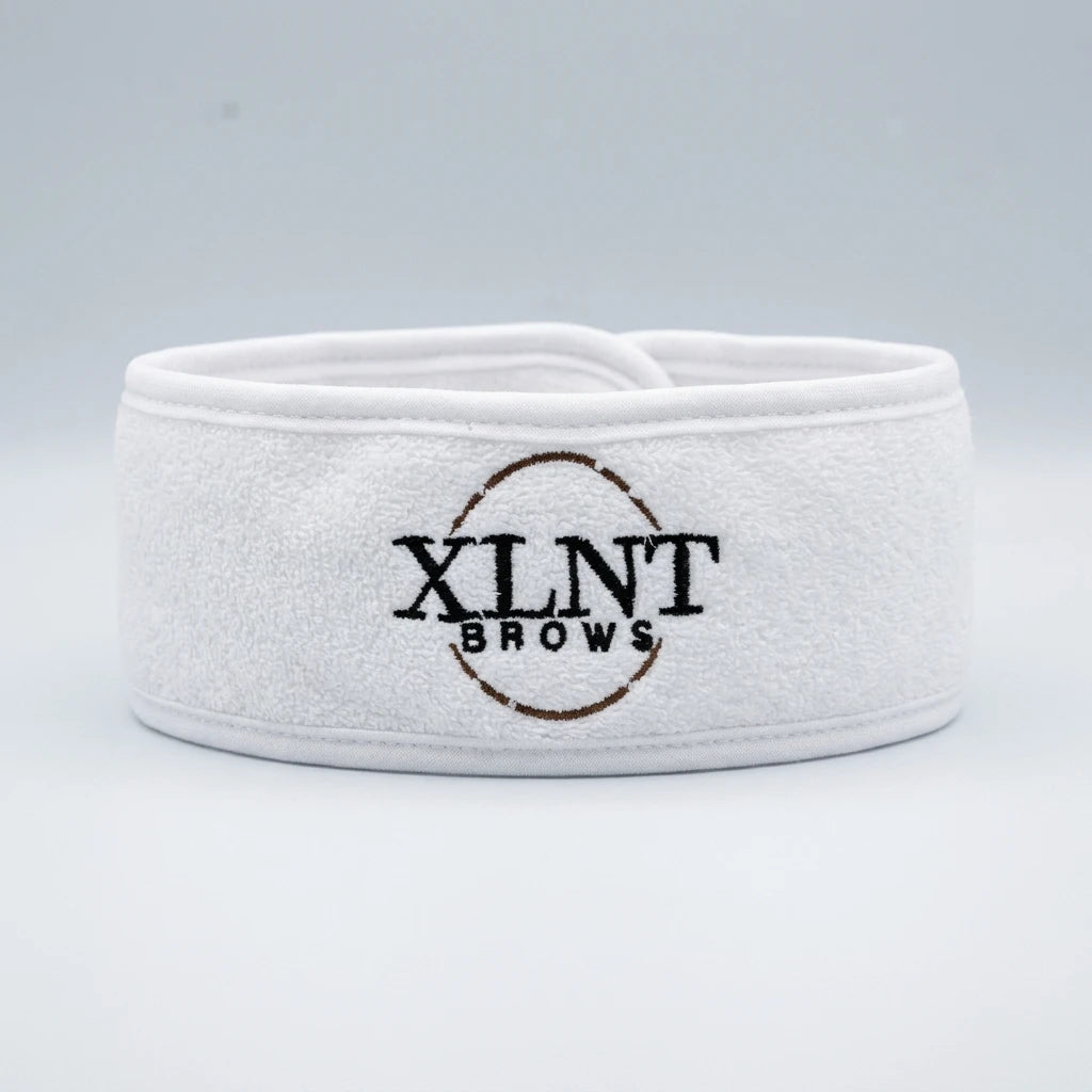 Vitt microfiberhårband från XLNT Brows med broderad logotyp mot ljusgrå bakgrund.