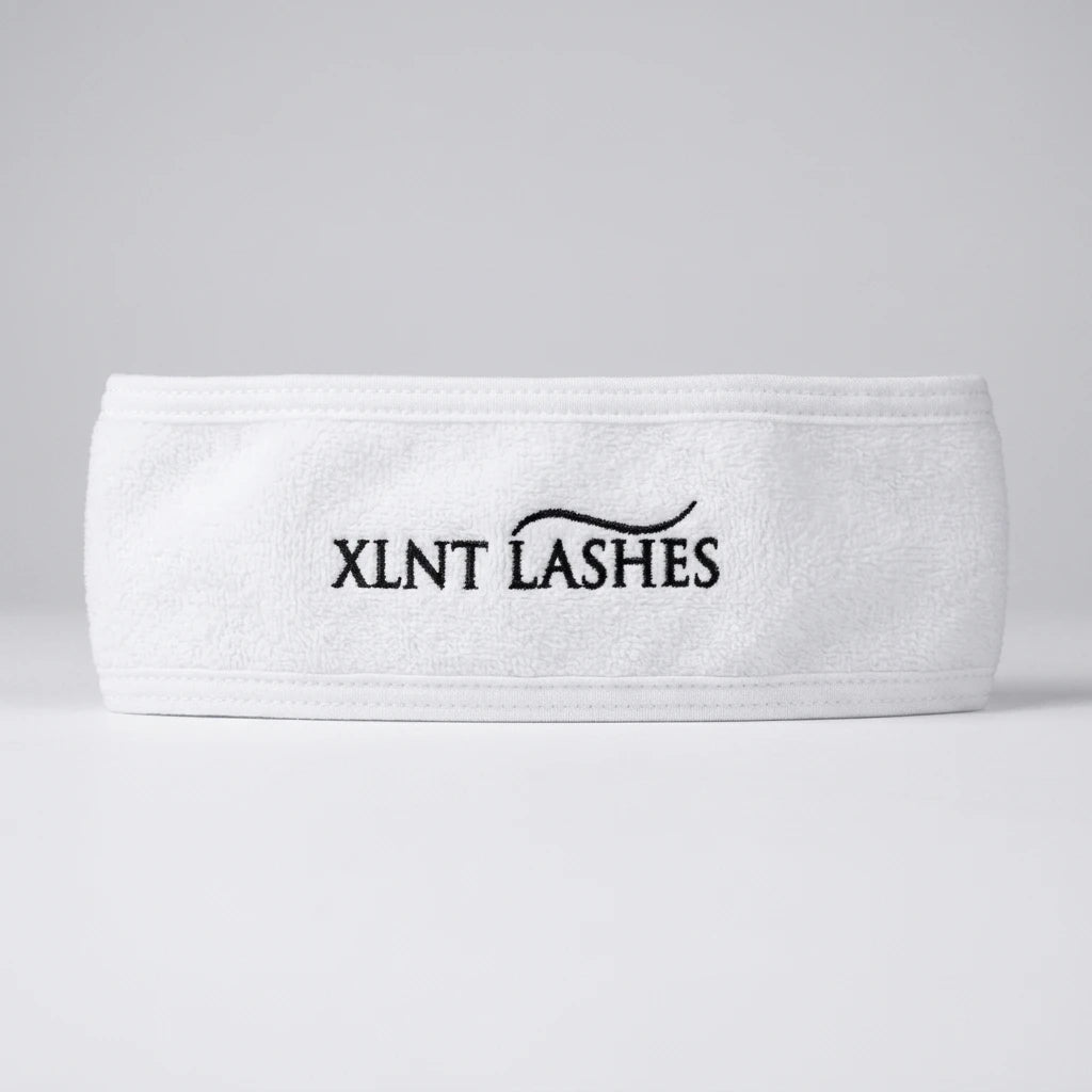 Brett vitt microfiber-hårband från XLNT Lashes med broderad logotyp mot ljusgrå bakgrund.