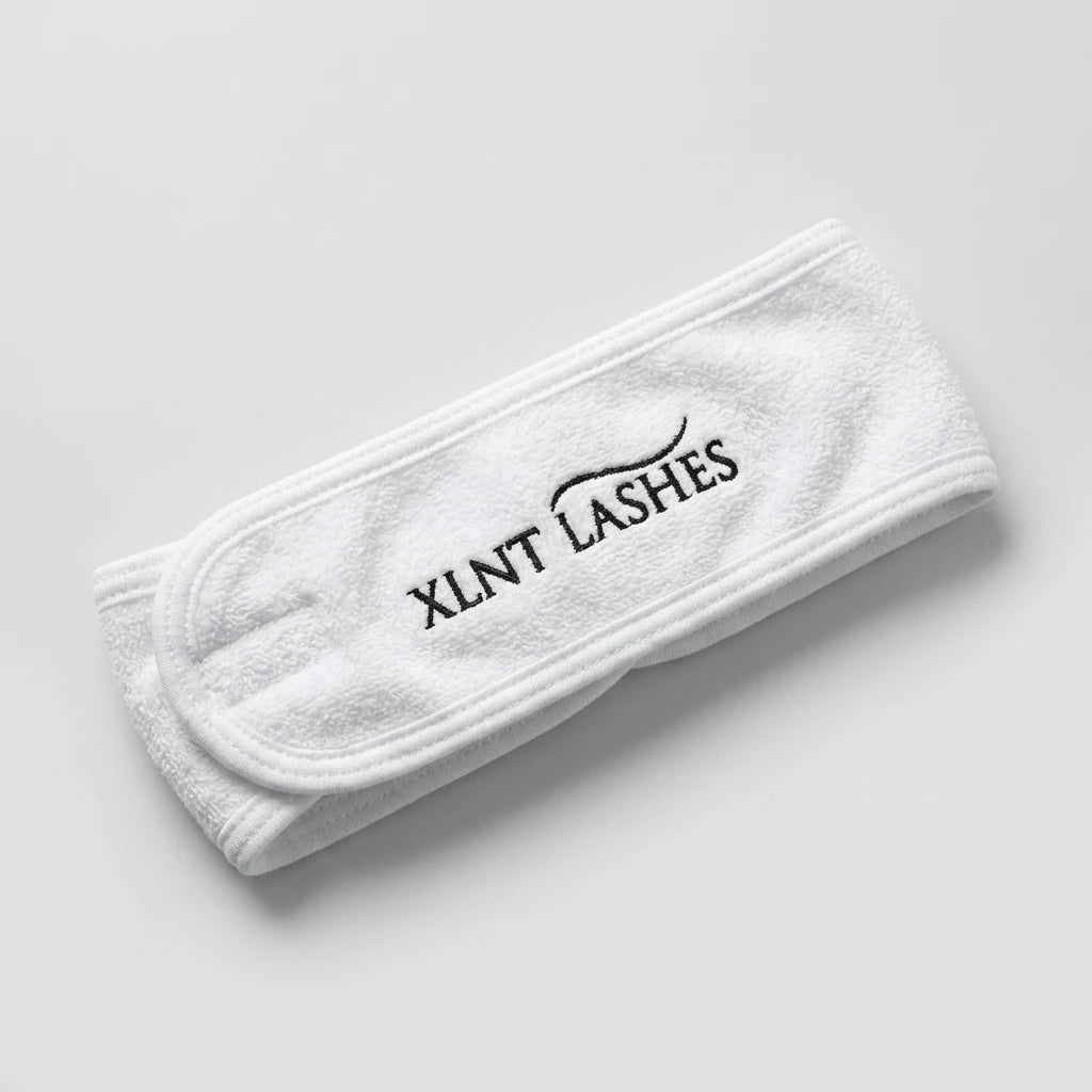 Närbild på XLNT Lashes microfiber-hårband i vitt med kardborreknäppning och broderad logotyp.