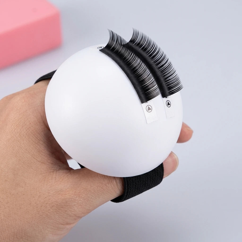 Lash Ball hålls i handen med två rader volymvippor placerade på den vita kupade ytan, redo för fransförlängning.