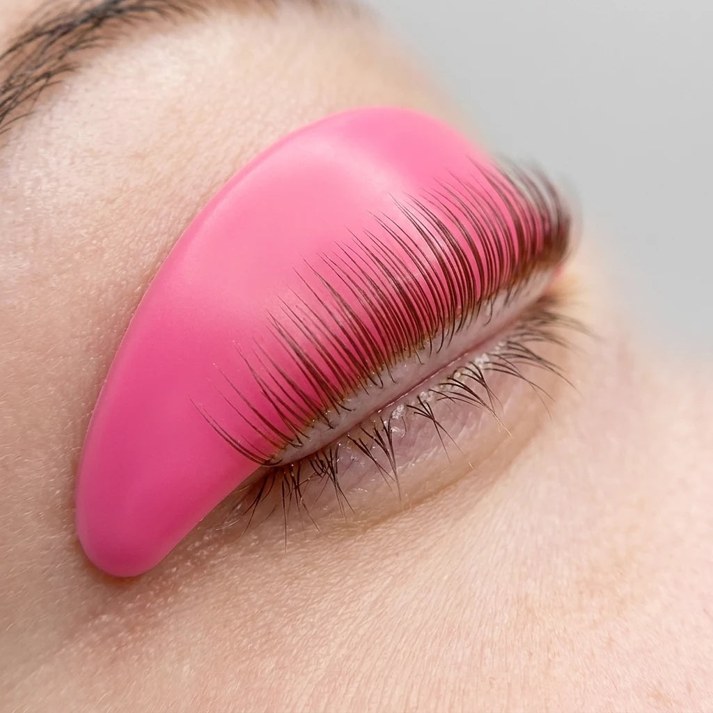 Rosa silikonpad placerad på ögonlock med uppkammade fransar under lash lift-behandling med L-böj.