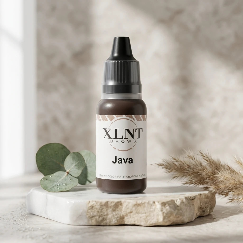 XLNT BROWS Java pigmentflaska på ljus stenplatta omgiven av eukalyptusblad – stilren salongsmiljö.