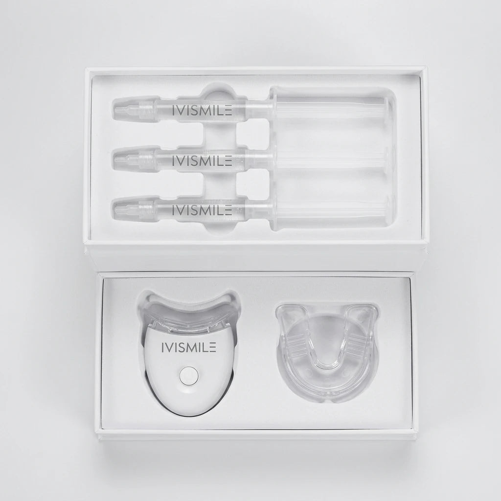 Tandblekningskit Ivismile Gold Kit med tre gelsprutor, vit LED-lampa och genomskinlig tandskena i en öppen vit ask.