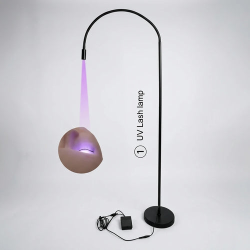 Mattsvart UV-LED-lampa med böjt golvstativ och fotpedal som lyser lila UV-ljus mot fransraden.